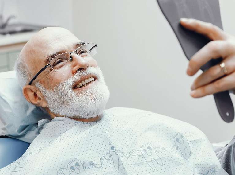 A smiling man looking at his dental implants in the mirror